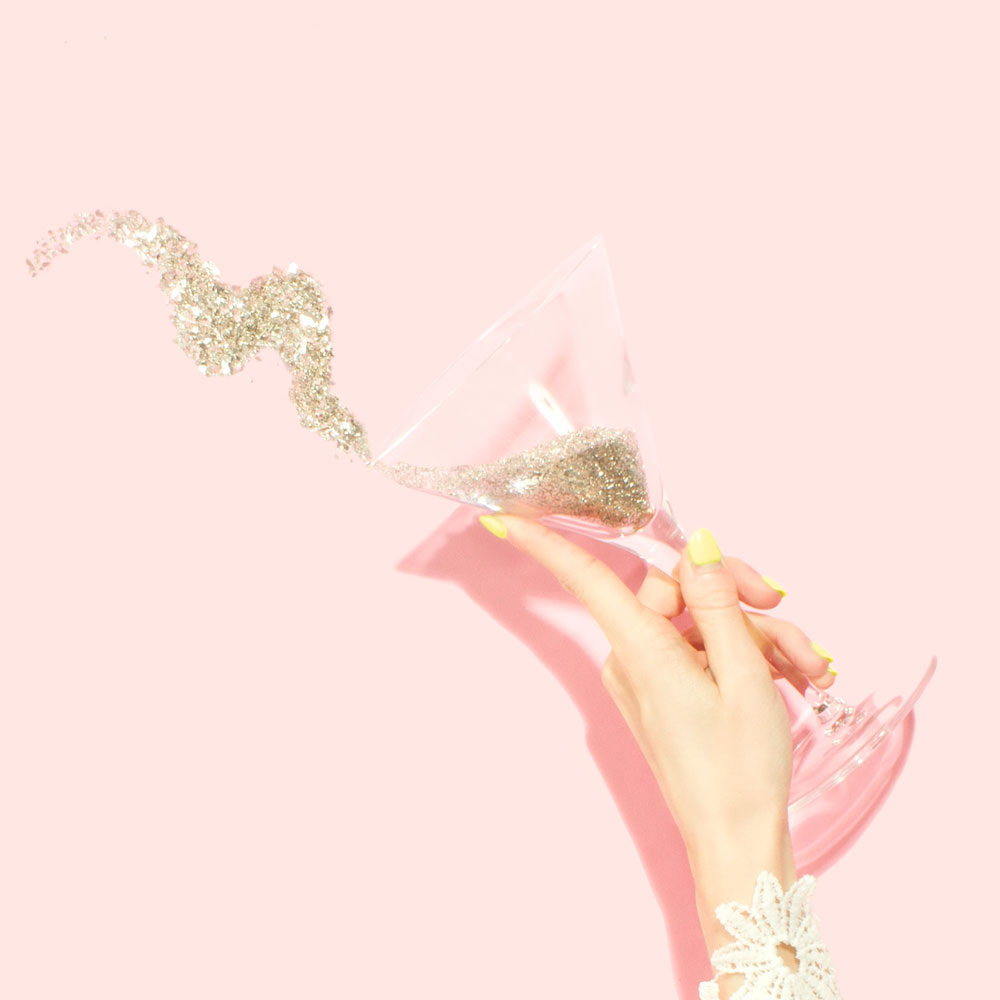 Woman's hand with manicured nails raises a martini glass filled with confetti